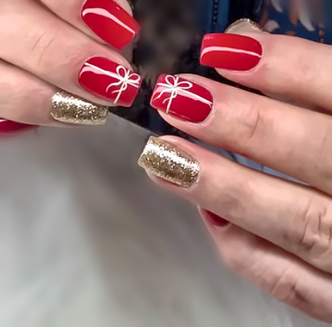 Red nails painted like wrapped gifts with gold glitter accent nails